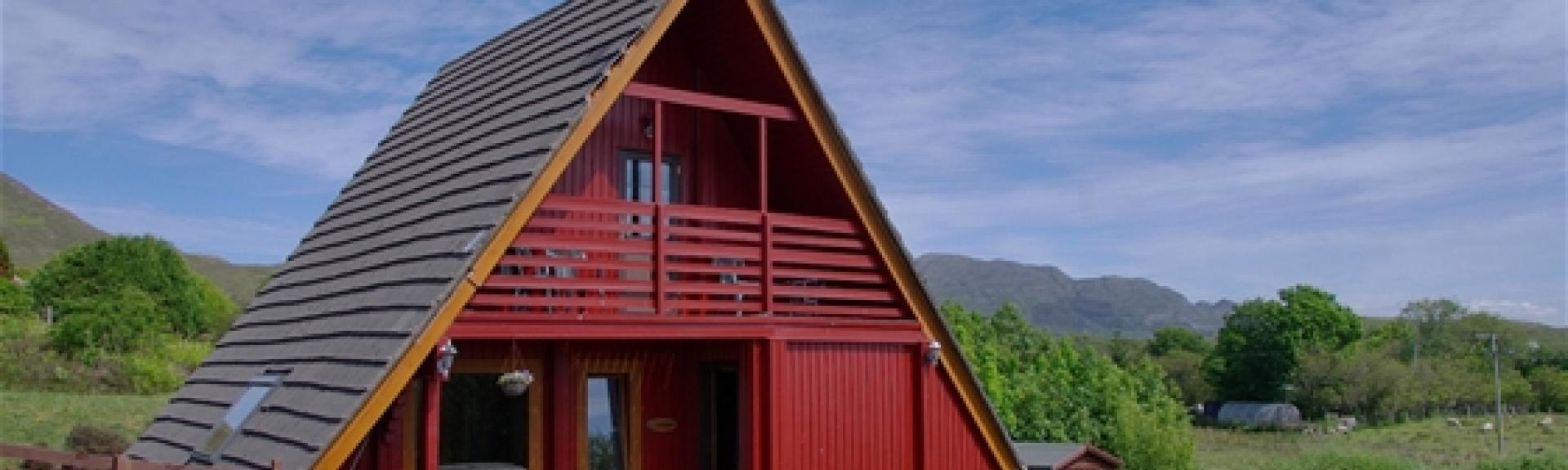 Exterior of a 2-storey, wooden A-Frame eco lodge surrounded by oprn countryside