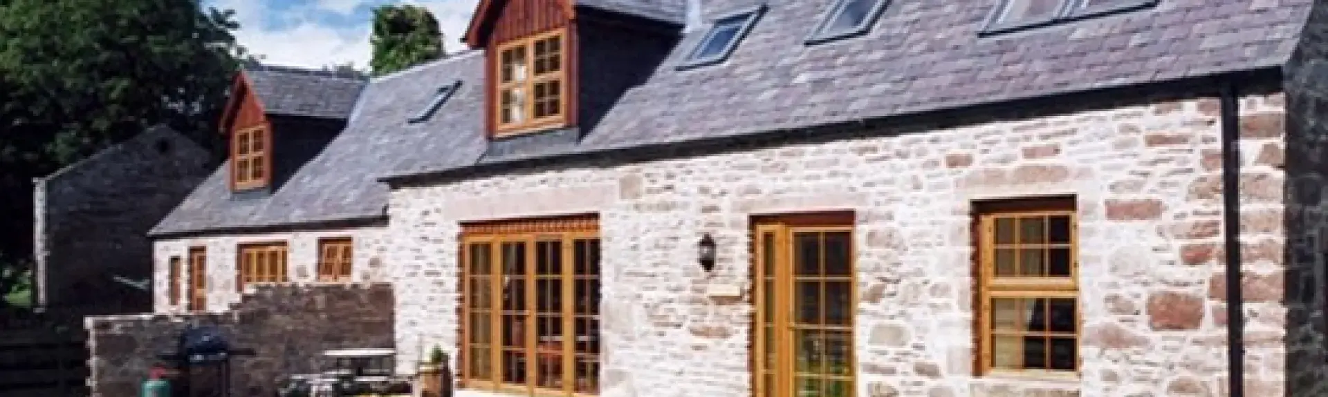 Exterior of a slate-roofed barn conversion with patio and lawned garden.