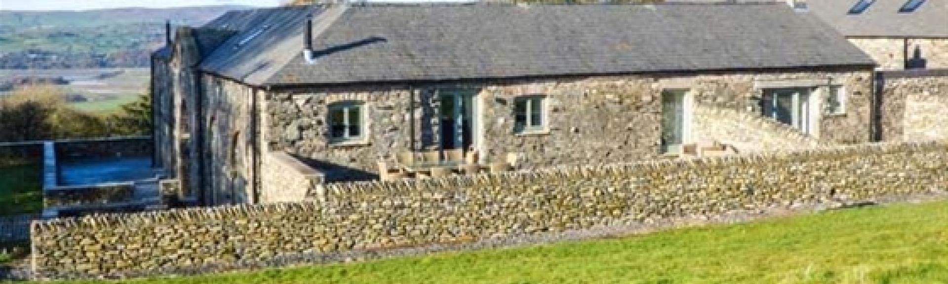 A single storey stone cottage sits behind a low stone wall.
