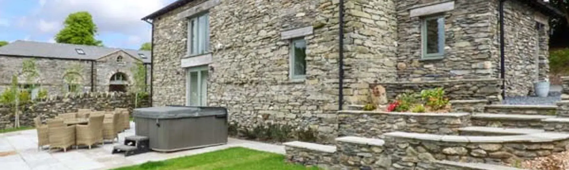 Stone-built estate cottage with a hot tub on its patio and a large lawn.