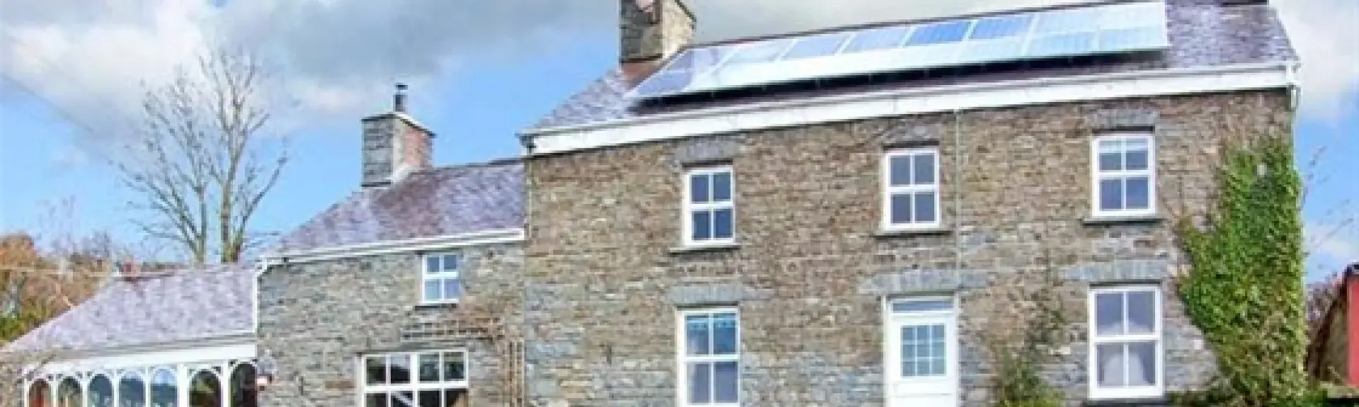 A detached, double fronted, stone-built cottage with a front garden behind a low stone wall.