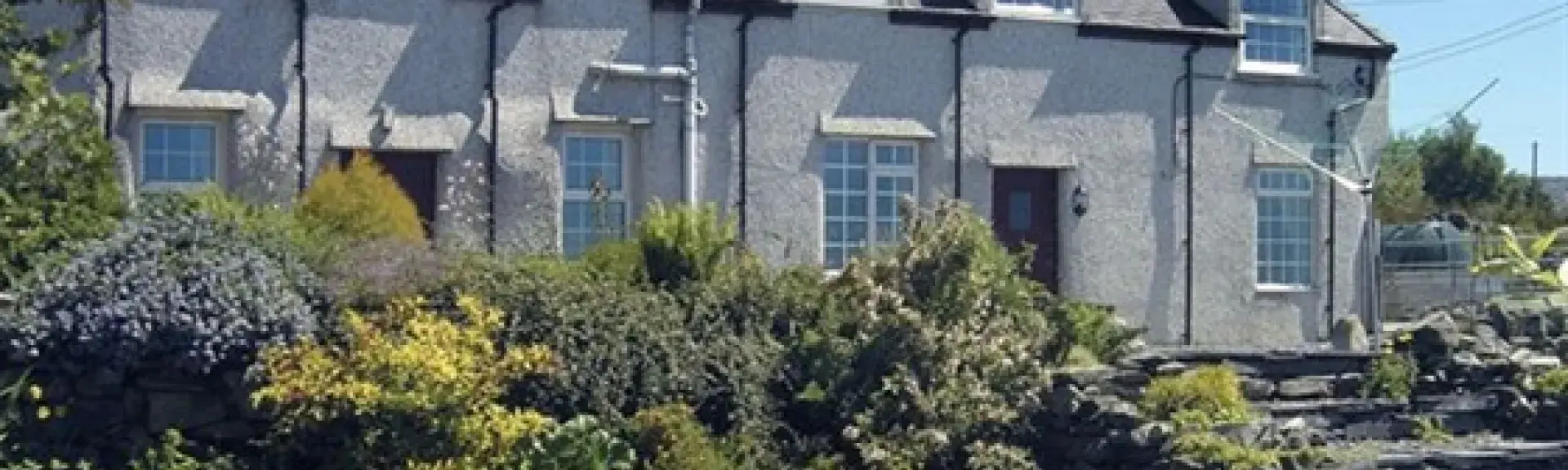 A row of terraced houses look down over a flower-filled rockery to a large lawn.