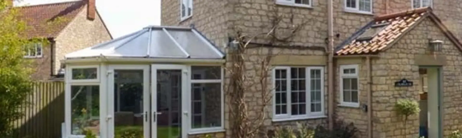 Exterior of a stone cottage with enclosed porch and sun lounge overlooking a lawn.