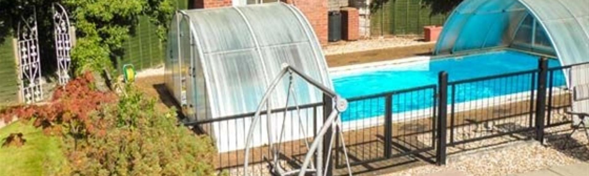 An outdoor swimming pool and terrace with a sun-lounger swing are overlooked by a garden and cottage. 