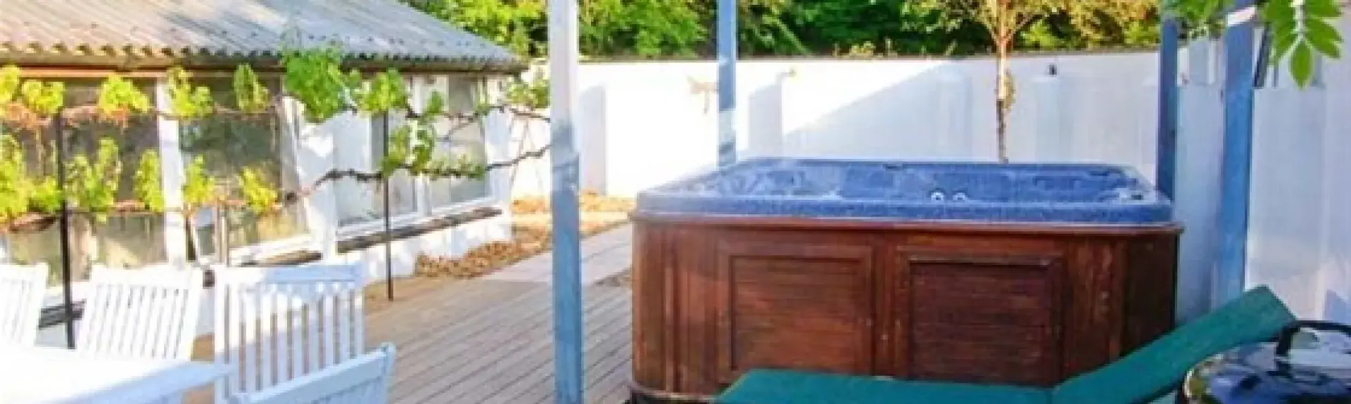 A hot tub beneath a glass roof sits on a wooden deck next to two sun loungers.