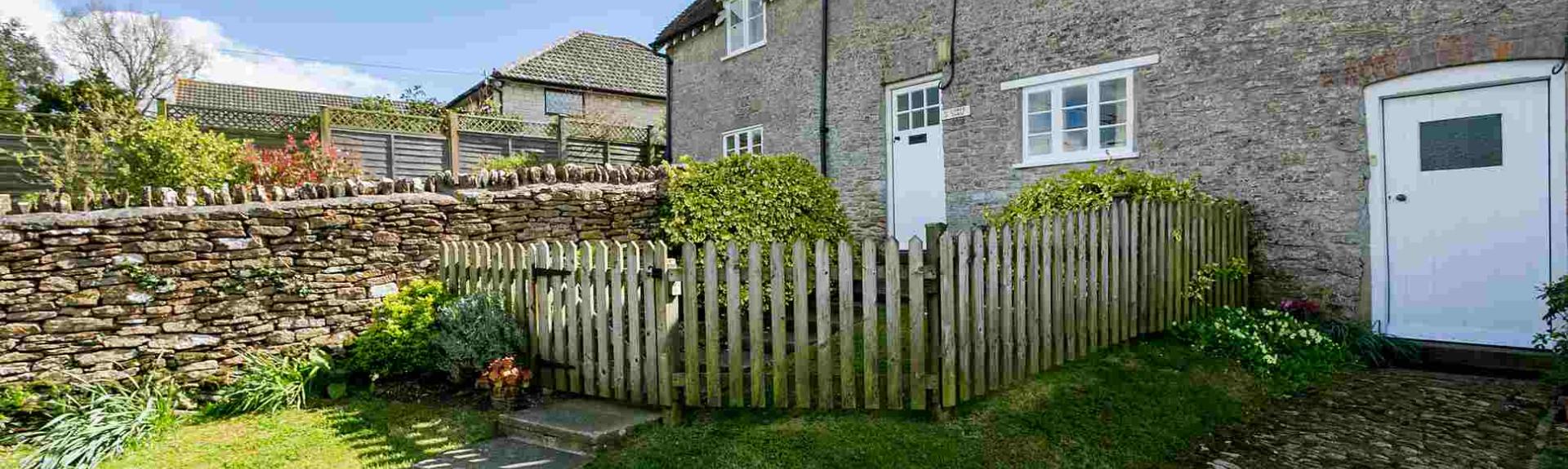 Exterior of a stone-built terraced cottage with a picket fence around the front garden.