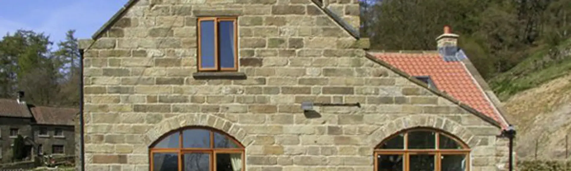 A stone-built North Yorkshire holiday cottage surrounded by woods and fields.