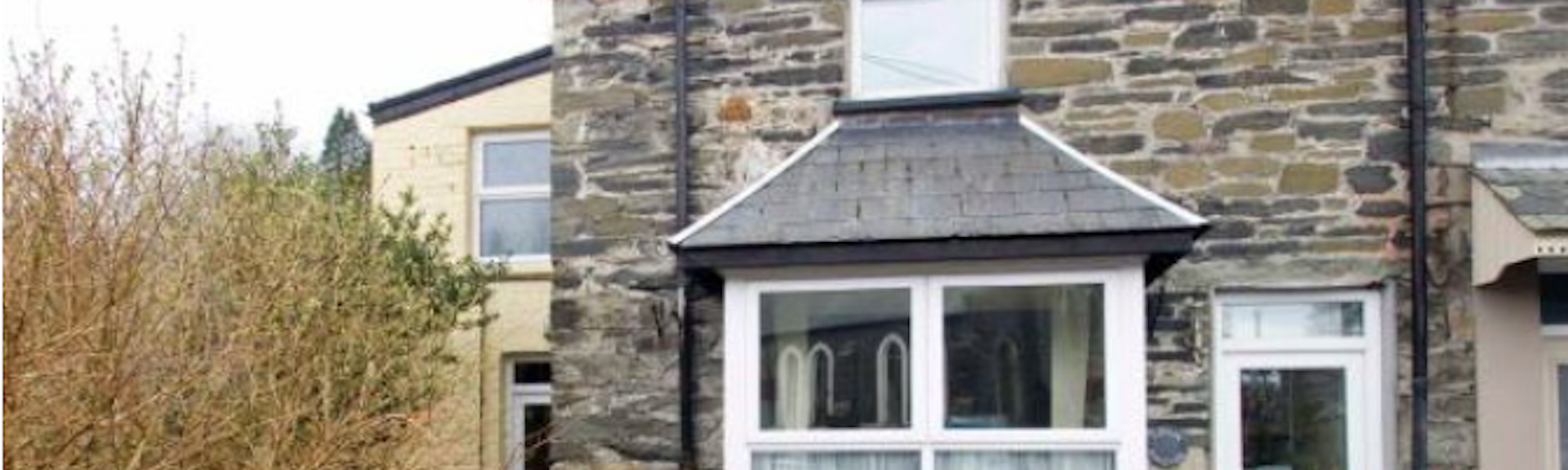 exterior of a stone-fronted holiday cottage in Snowdonia with a slate r.oofed bay window