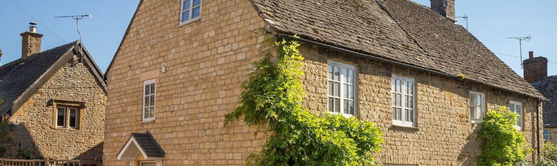 A semi-detached Cotswold honeystone cottage with wisteria-clad walls
