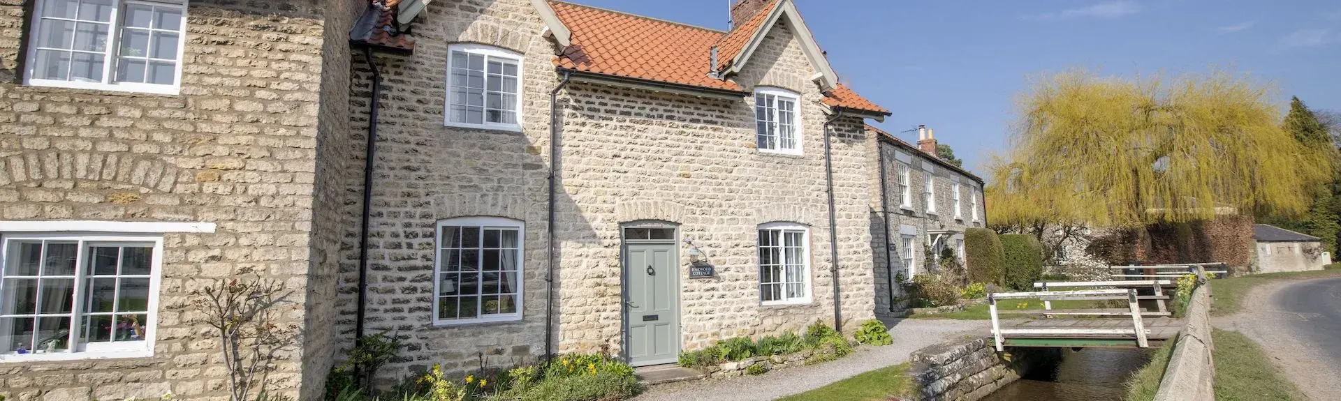 A stone built holiday cottage in Hovingham overlooks a steam running past its frontage on a summer's day.
