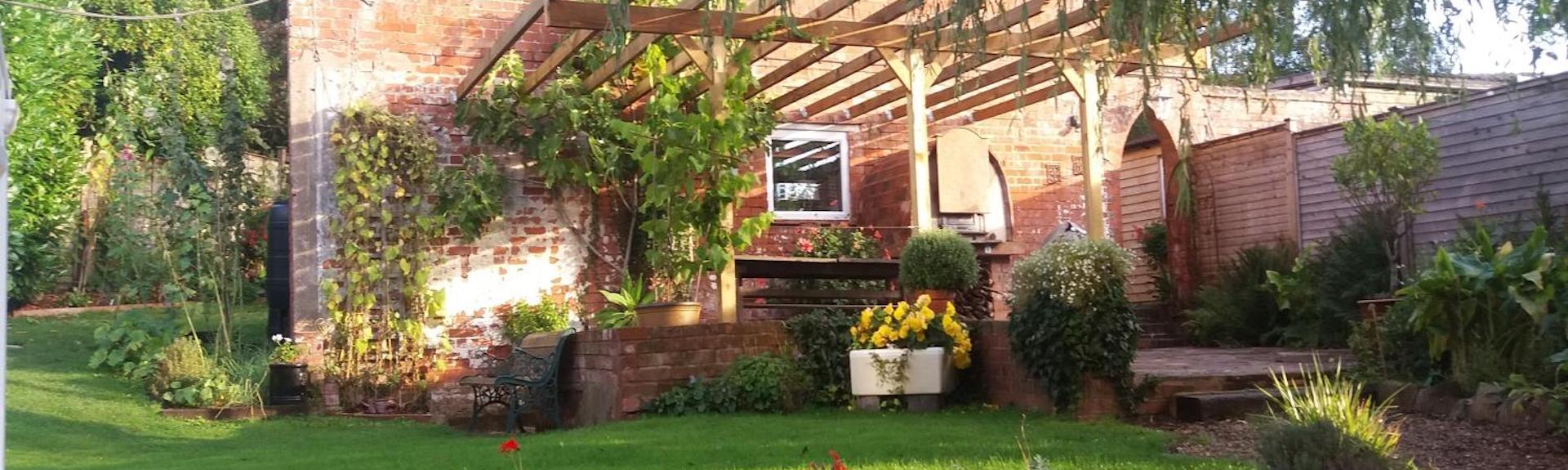 Exterior of a single storey holiday apartment with a vine covered pergola and floral garden.