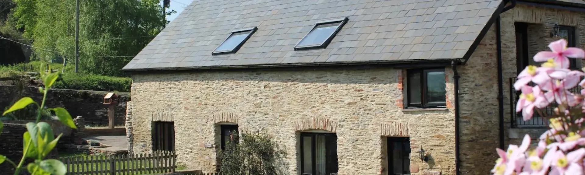 Exterior of a sonte-buklt Exmoor holiday cottage with a background of trees and a clear sky