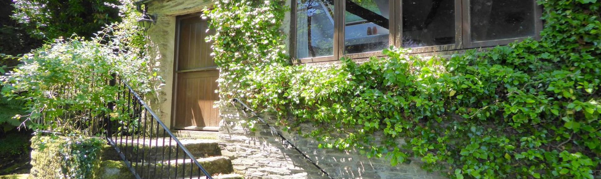 the leafy-clad exterior of a stone-built single-storey exmoor holiday cottage with a flight of stone stteps to the front door