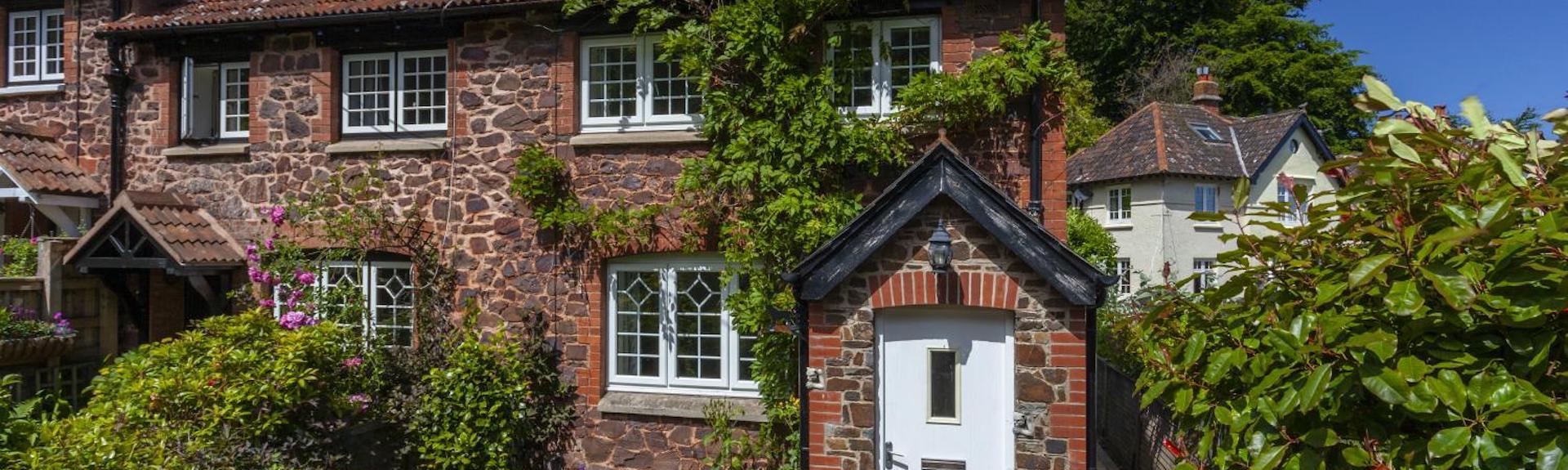 Exterior of a wisteria-clad stone-built holiday cottage in Porlock on a sunny day.