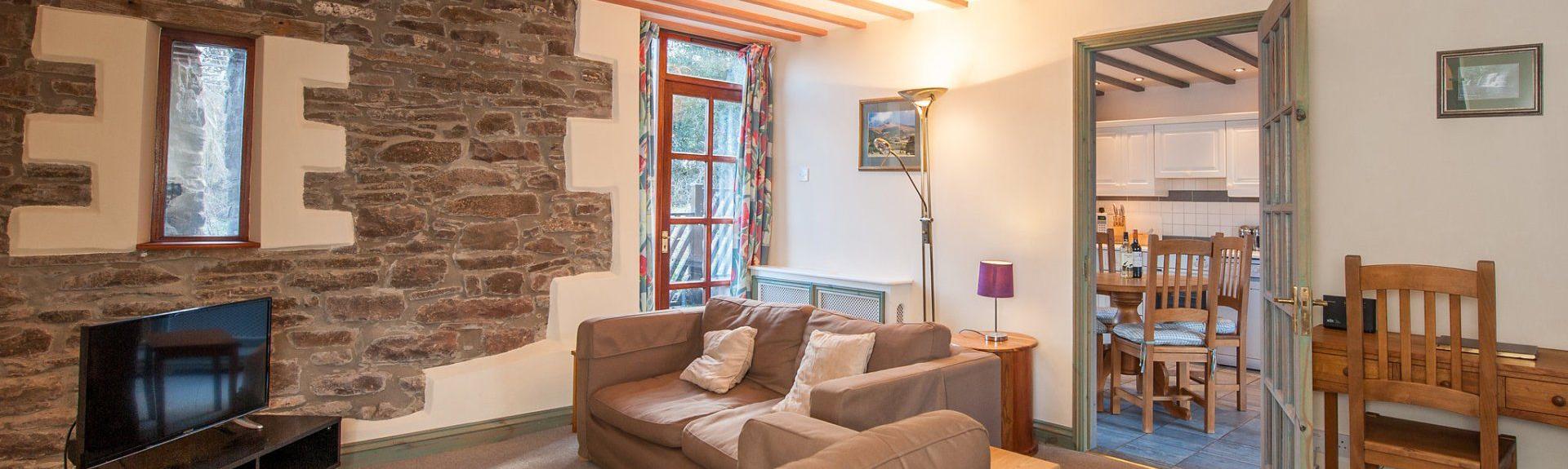 A holiday cottage lounge with exposed stone walls, pine beams and comfortable sofas.