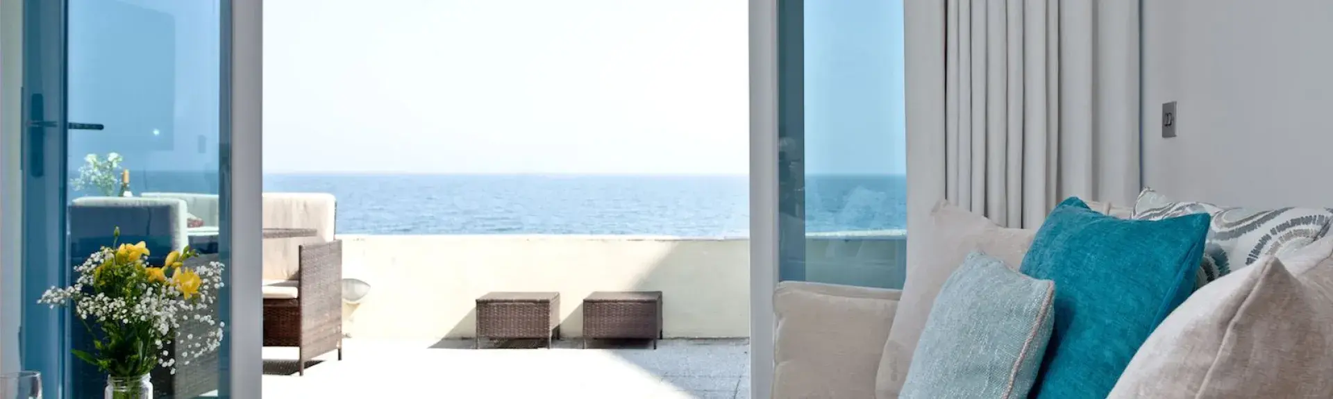 A lounge with comfortable sofas and TV has French windows with a sea view
