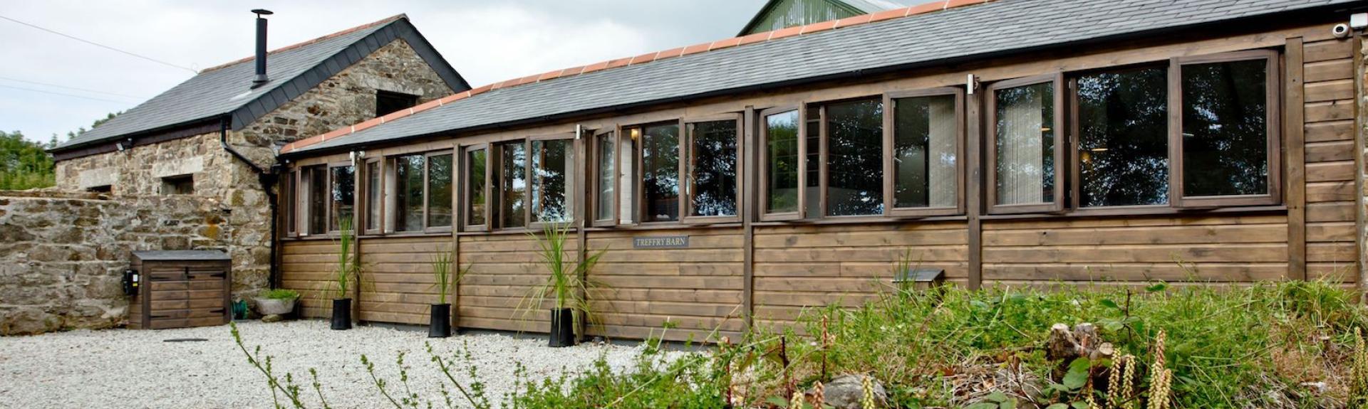 A long single-storey barn conversion with a line of windows along one side overlooks a shingled driveway and garden.