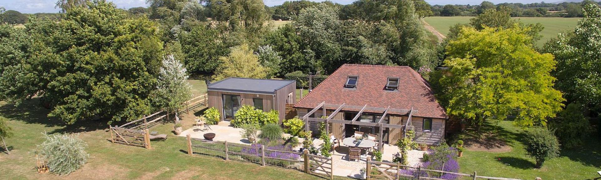 A 2-storey barn conversion with  terracotta tiles nestles against a cluster of small trees overlooking a large garden and fields in East Sussex.