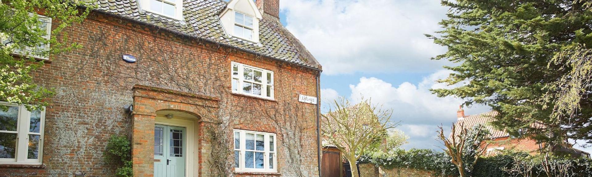 Exterior or an old 3-storey country cottage in Norfolk overlooking a large lawn bordered by mature trees.