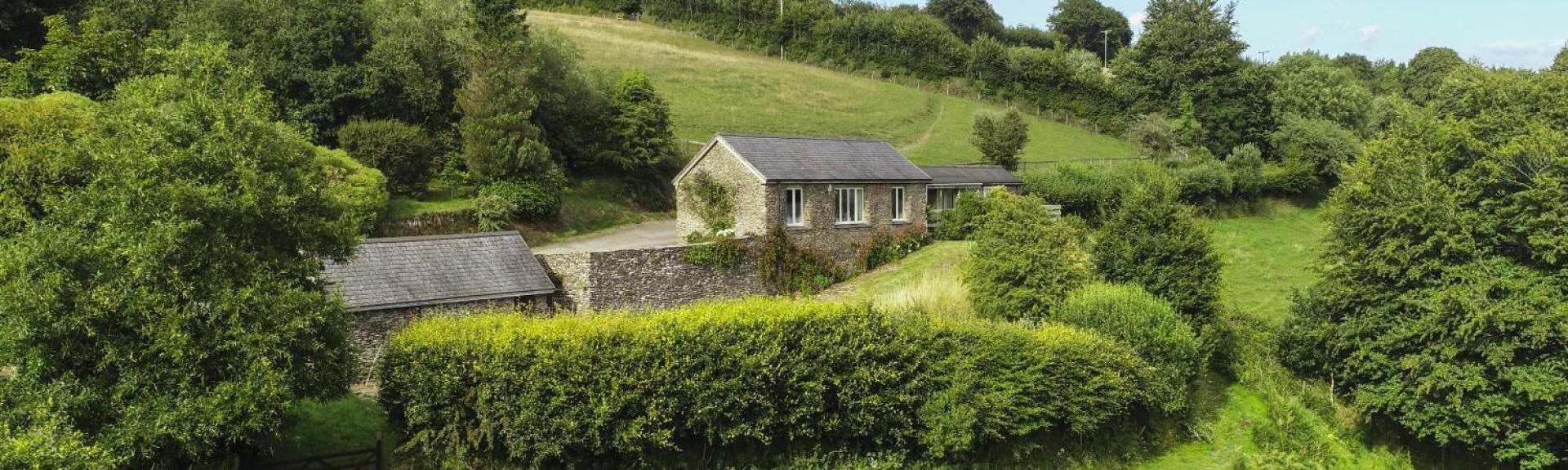 A remote hillside lodge on the side of a hill surrounded by fields,hedgerows and trees.