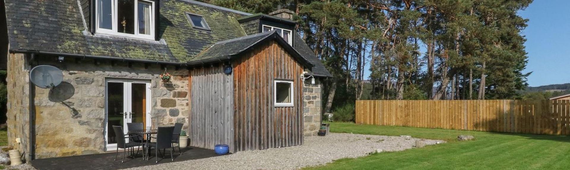 Backed by tall pine trees a 2-storey tone-built Newtonmore holiday cottage overlooks a large lawn.