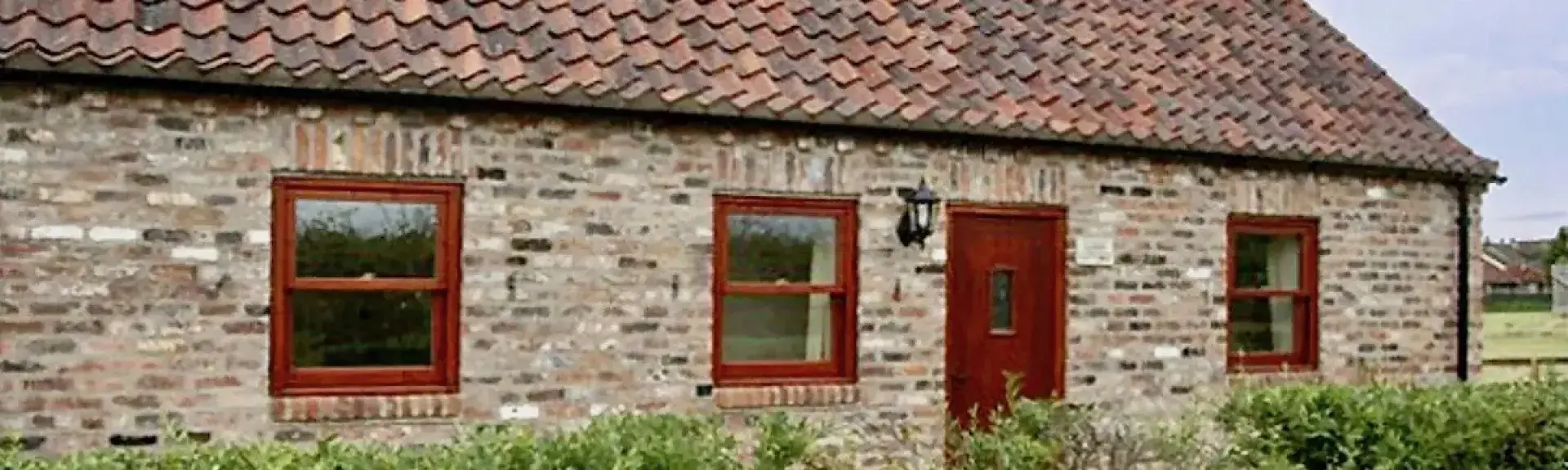 Exterior of a single-storey stone-built rural holiday cottage with a terrace and a front hedge.