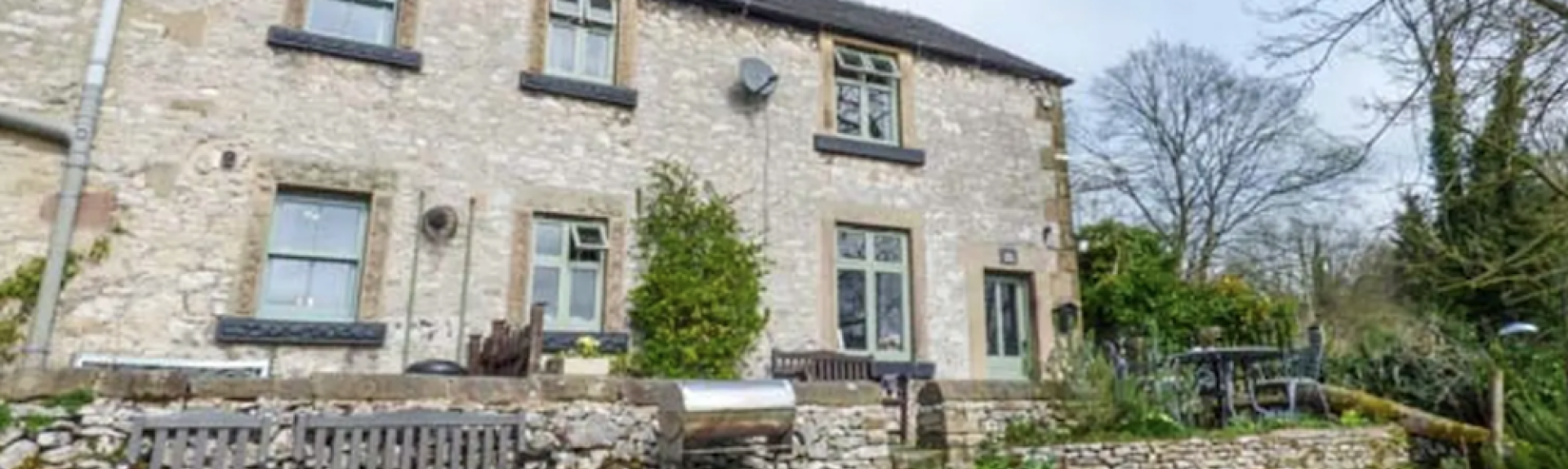 Exterior of a 2-storey stone-built holiday cottage in Derbyshire overlooking a large lawn.