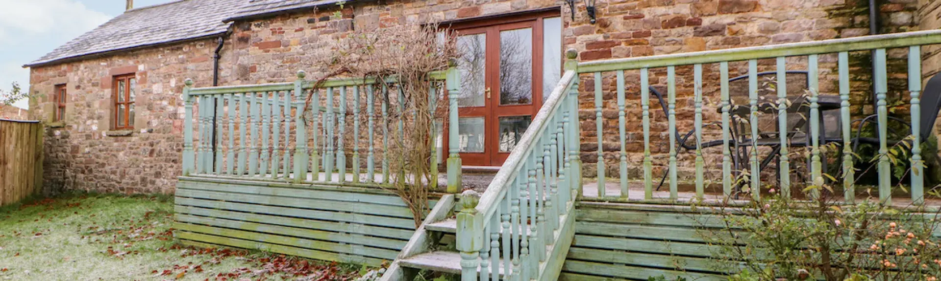 Single-storey brick-built barn conversion forming a holiday cottage with a long deck and lawned garden with a light sprinkling of winter snow. overlooking a