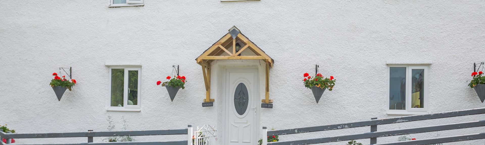 Front exterior of a double-fronted2-storey  Welsh holiday cottage with wall-mounted flowerpots and a wooden fence.
