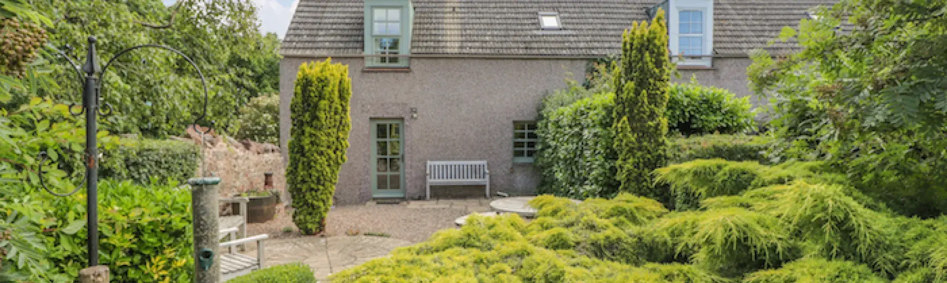 A small holiday cottage in St. Abbs sits behing a flourishing garden of small trees,sshrubs and a winding garden path.