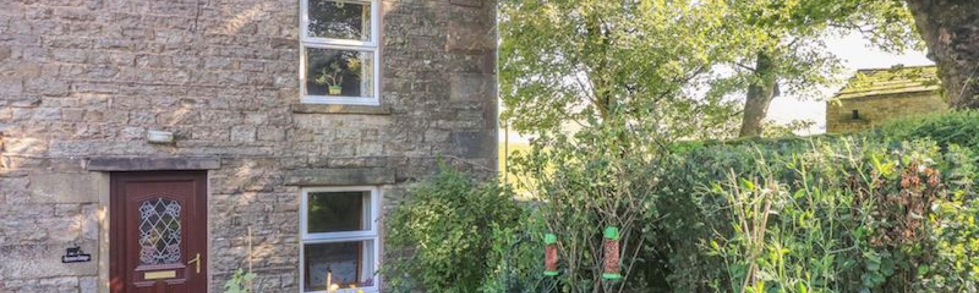 A stone built country cottage in the Yorkshire Dales overlooks a mature garden with flowering poppie.