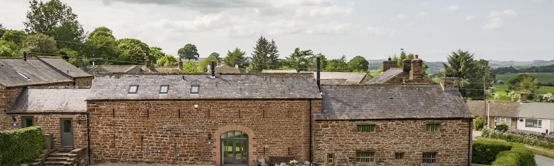 Exteriorof a large stone-built hall in Cumbria with a large lawn and parking spaces.