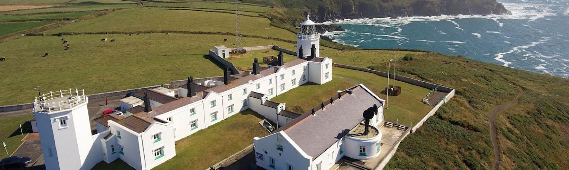 Aerial view of a Lighthouse and crew buildings atop cliffs overlooking the sea at Lizard Point in Cornwall.