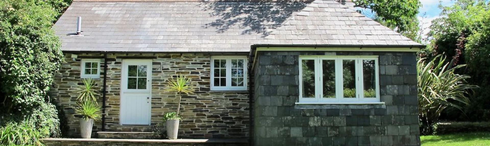 Granite-built exterior of a single storey Cornish holiday home surrounded by lawns.ottage