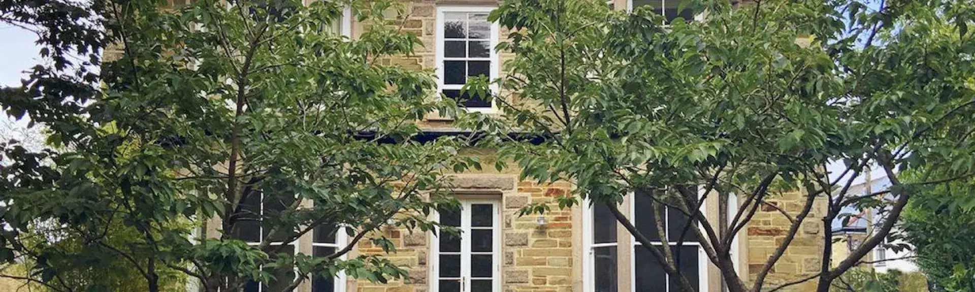 Double-fronted stone exterior of a Cornish cottage with bay windows and a terrace for outdoor dining.