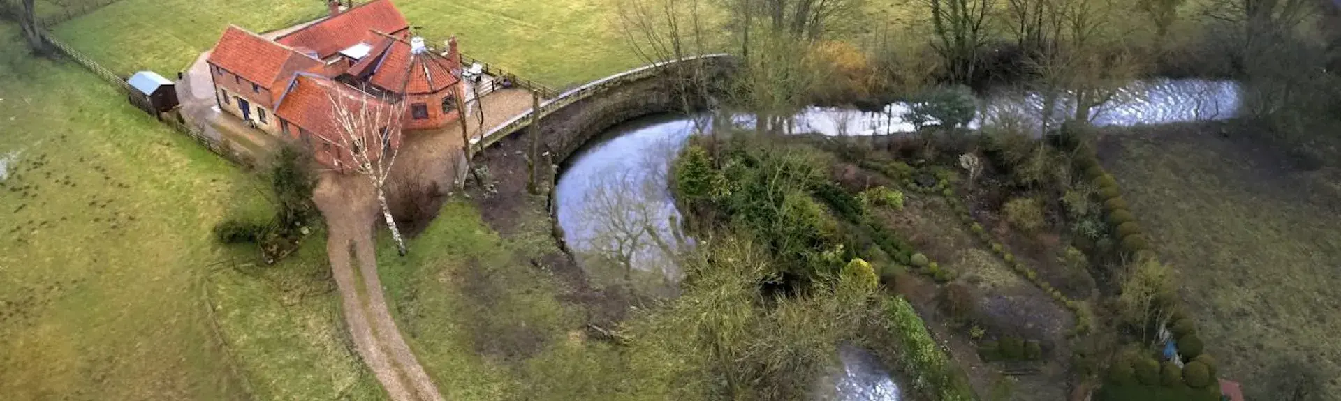 A farmhouse and attached barns in open countryside overlook a bend in a river