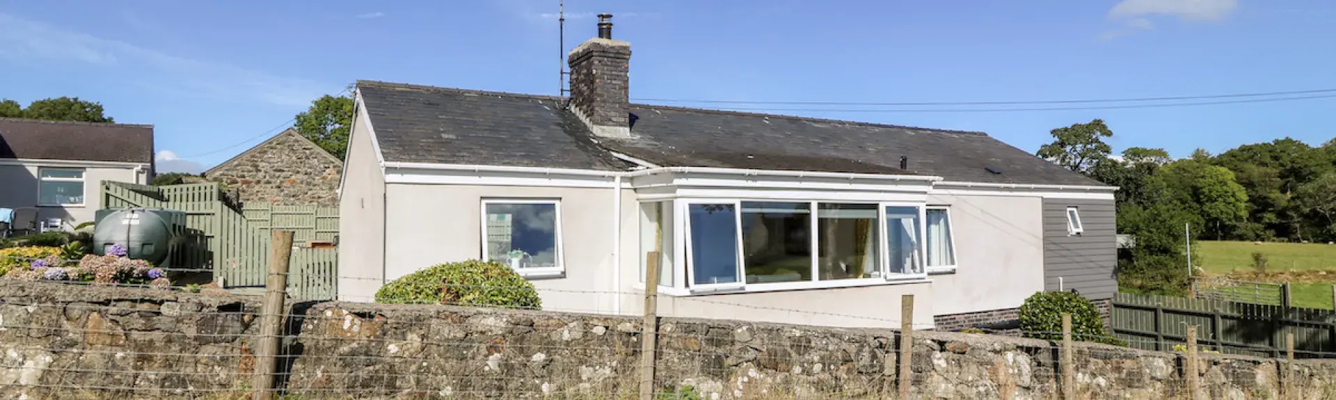Exterior of a modern bungalowsurrounded by a low stone wall and surrounded by open fields.