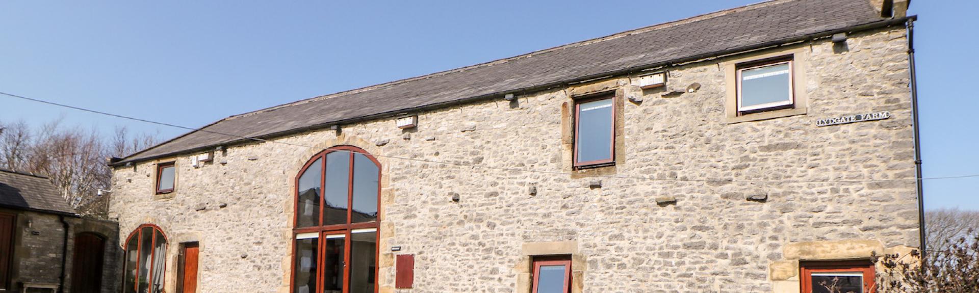 Exterior of a long, stone-built barn conversion in Priestcliffe, overlooking a courtyard and a walled garden.