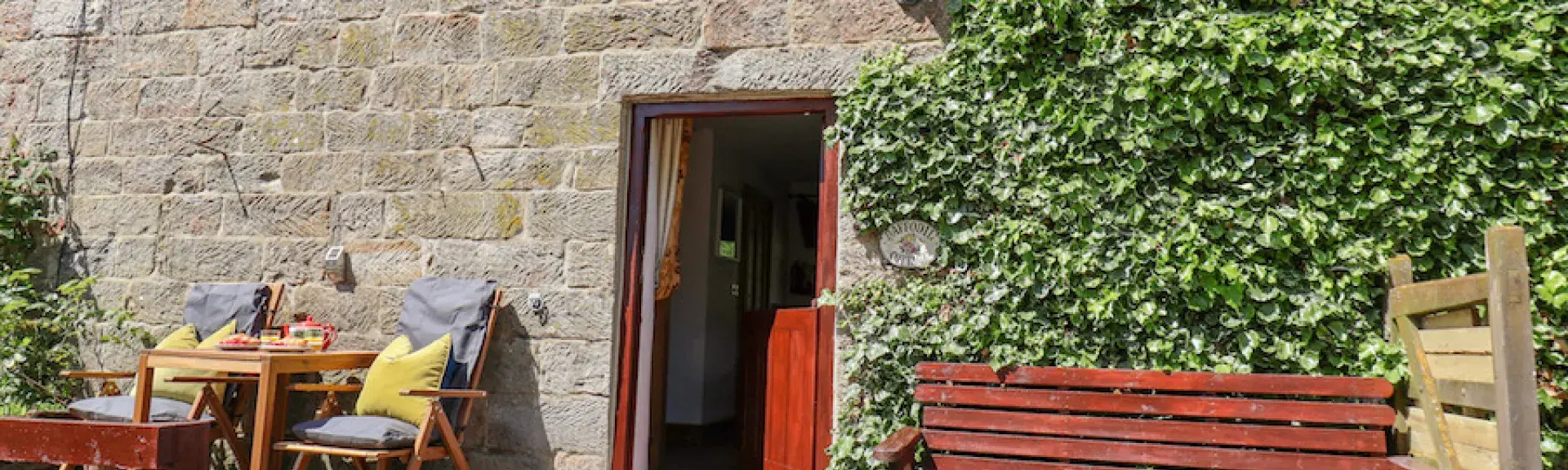 A cosy stone-built cottage in Danby on a sunny day with a garden bench and patio.
