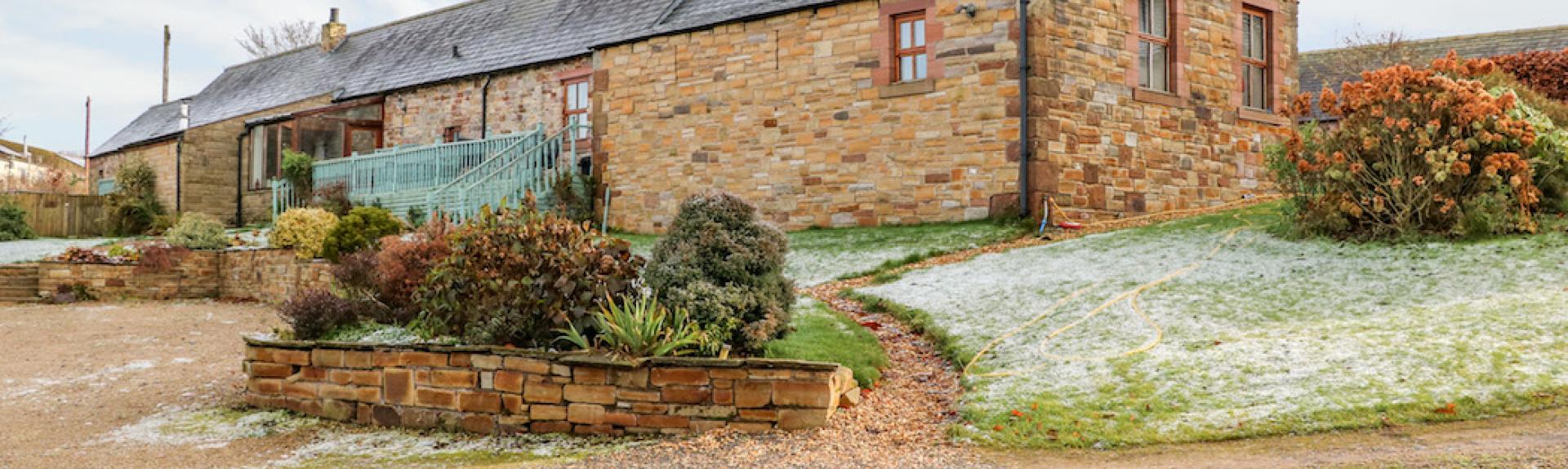 A single-storey, stone-built barn conversion in Cumbria with parking spaces and lawns.