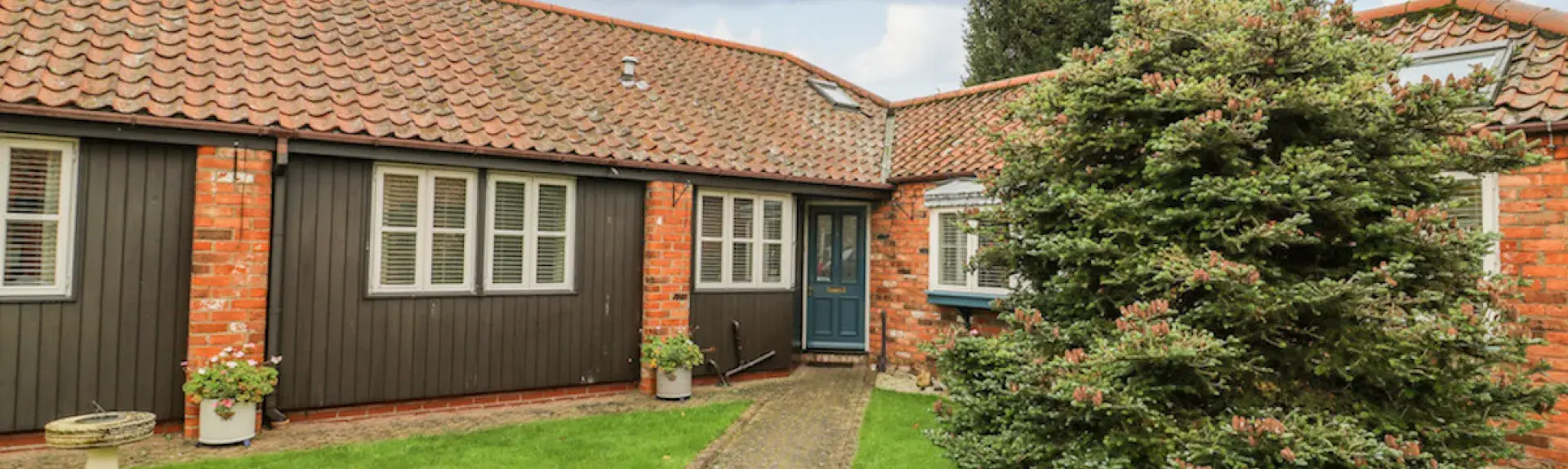 A single-storey wooden brick path crosses a lawn to the front door of wooden barn conversion 
