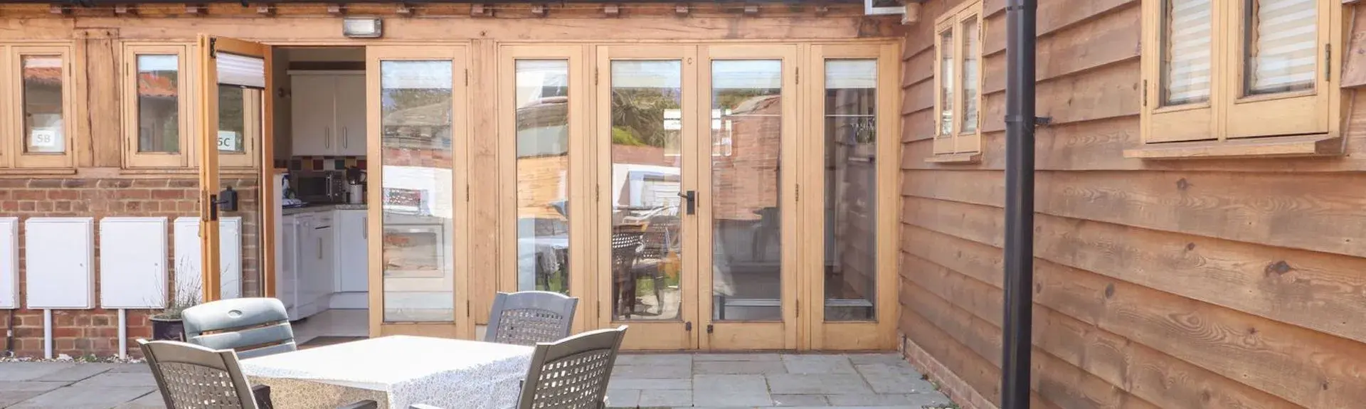 L-shaped exterior of a wooden barn conversion with floor-to-ceiling folding windows.