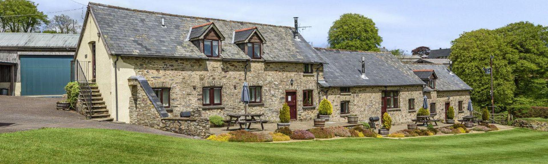 Exterior of a stone-built Exmoor Holiday Cottage surrounded by spacious lawns.