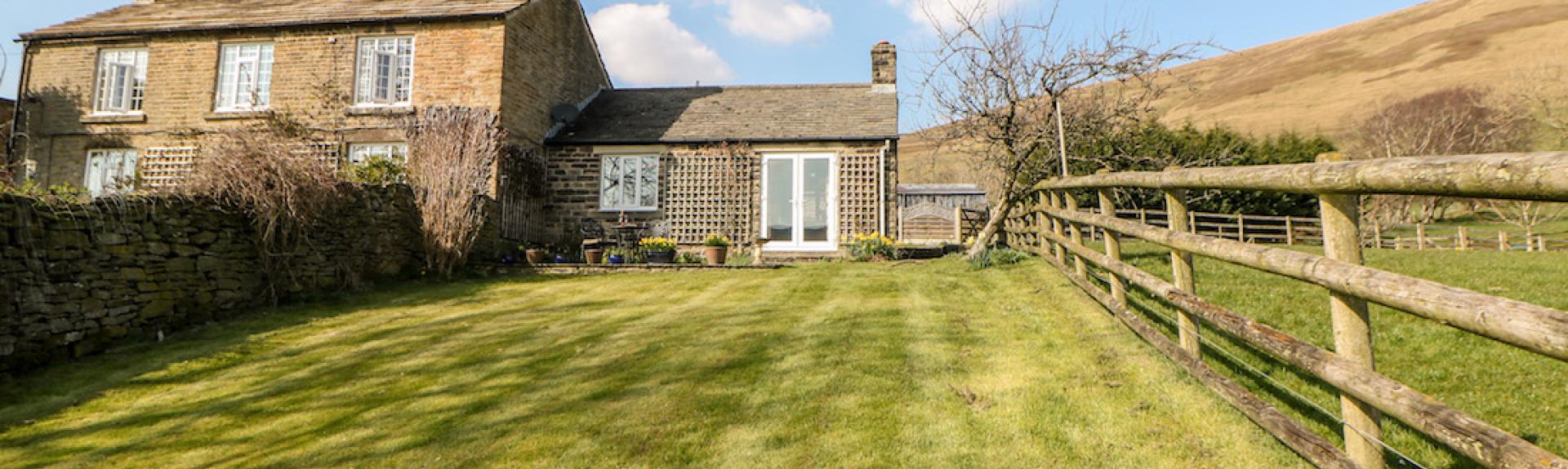 A large cottage with a ground floor extension is surrounded by open fields and moorland.