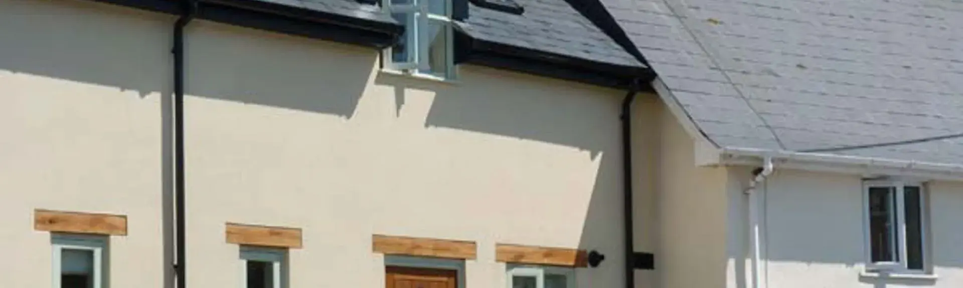 A two-storey converted bakery cottage behind wrought-iron railings in an elevated position above a village street.