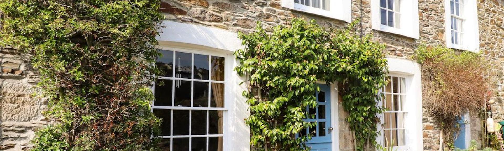 Exterior of a wisteria-clad, terraced holiday cottage in Mevagissey overlooking a cobbled street.
