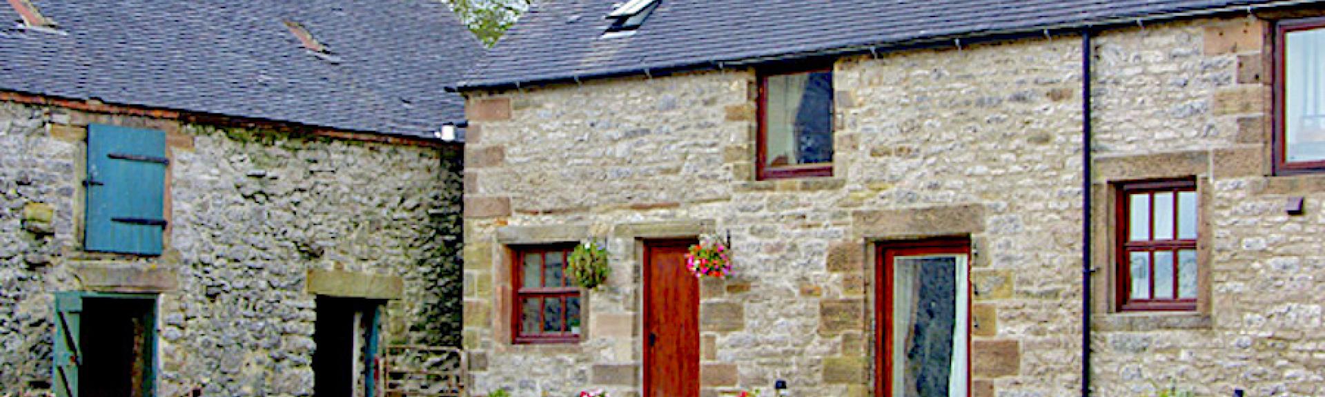 A stone-built cottage overlooks a cobbled courtyard bordered by a low stone wall.