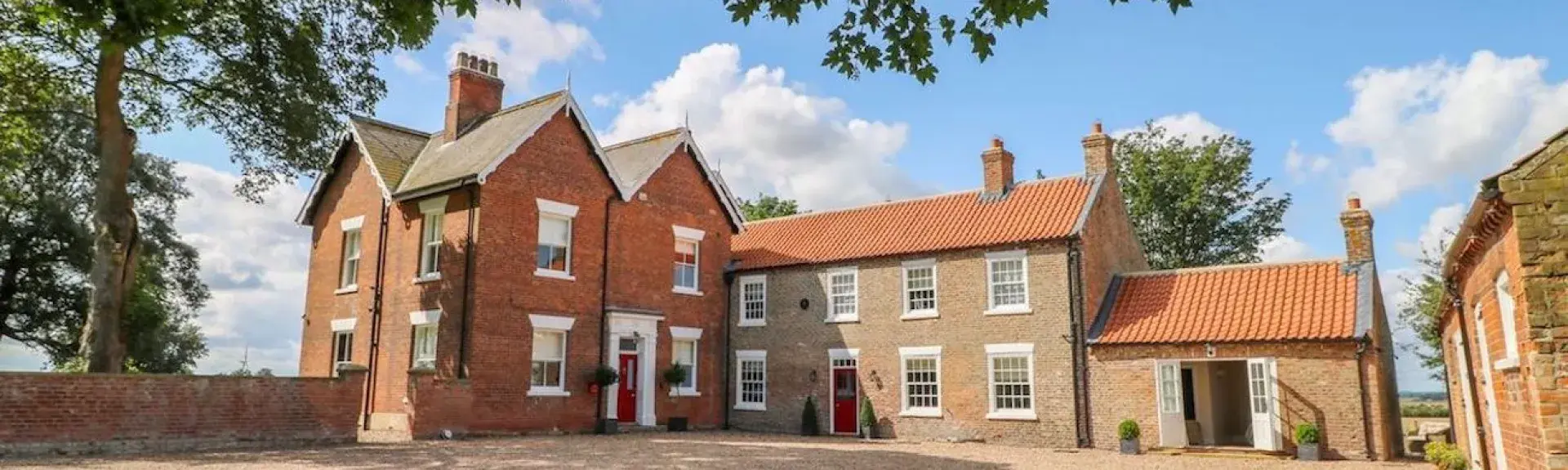 Exterior of a large, L-shaped brick East Yorkshire farmhouse overlooking a spacious courtyard and lawn.