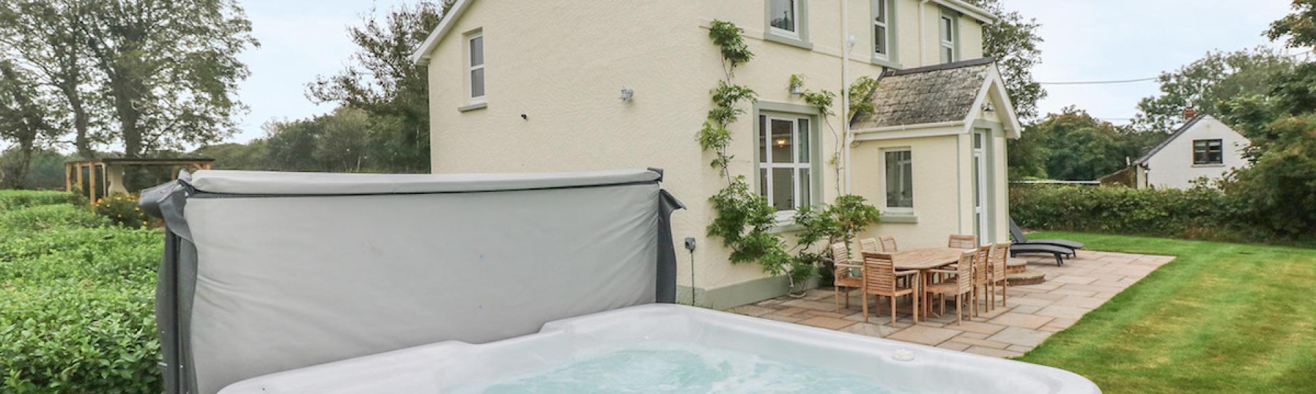 A hot tub bubbles away i in front of an elegant Pembrokeshire holiday cottage surrounded by  a patio and lawns.