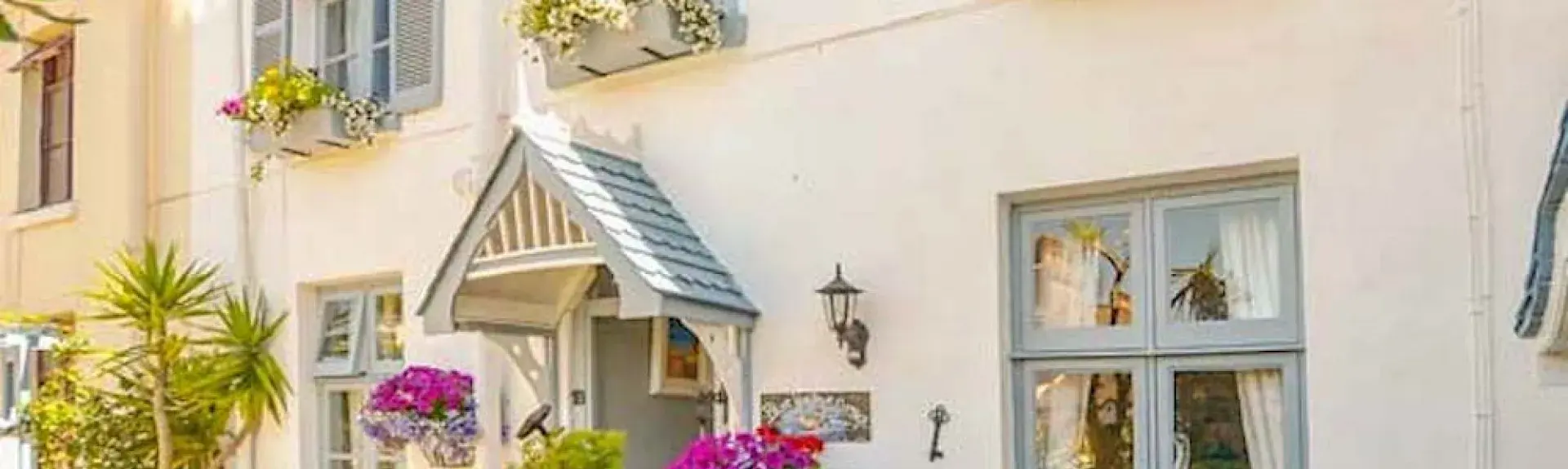 Exterior of a double-fronted Torquay holiday cottage with a small overhead porch and flower-filled front garden.